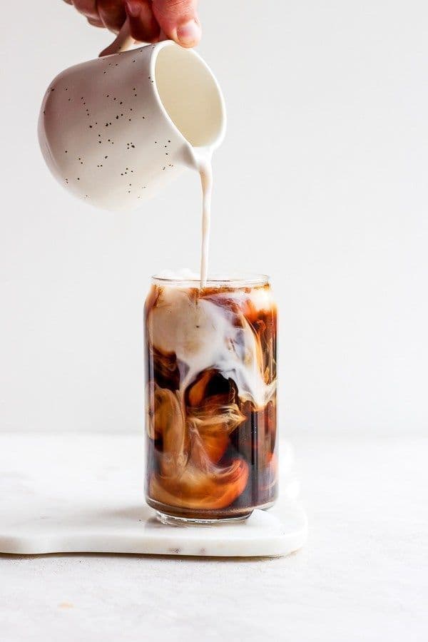 Cream poured from a speckled jug into a glass of cold brew.